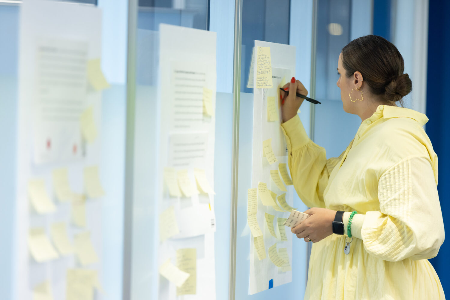 A woman writes on a post-it note on the wall.