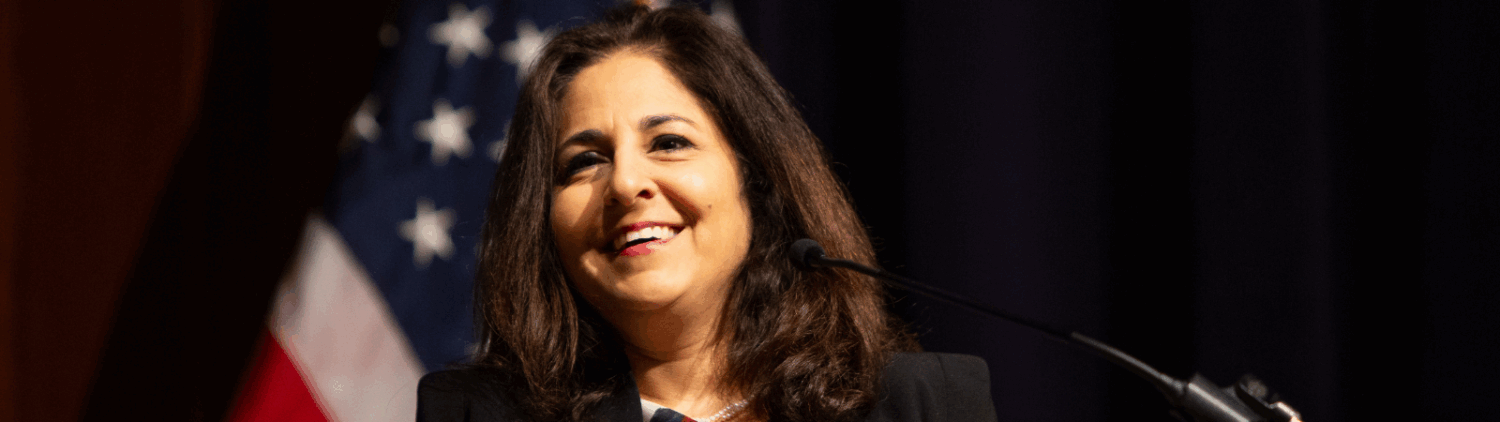 Woman speaks at a podium with an American flag behind her.
