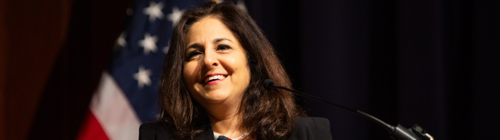 Woman speaks at a podium with an American flag behind her.