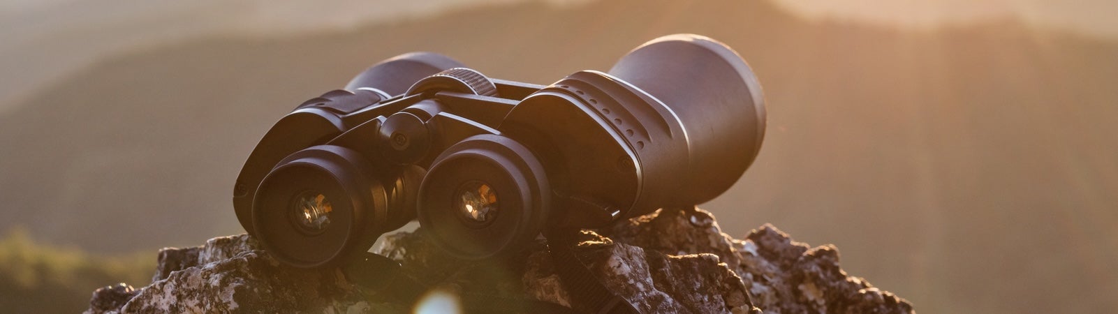 A photo of binoculars resting on a rock and pointed toward a sunrise over the hills. It represents AI futures worth building.