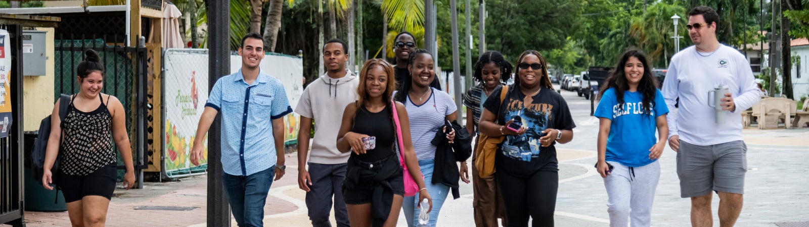 A group of diverse young adults walks on a sidewalk, smiling.