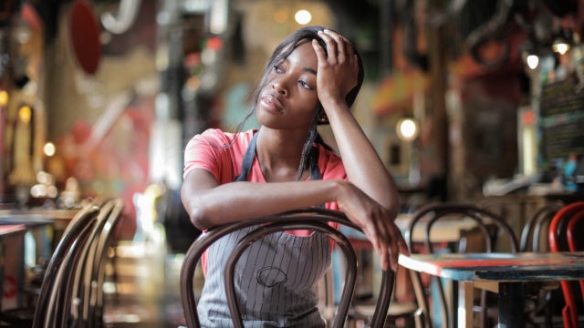 Restaurant worker sits in an empty restaurant, looking sad.