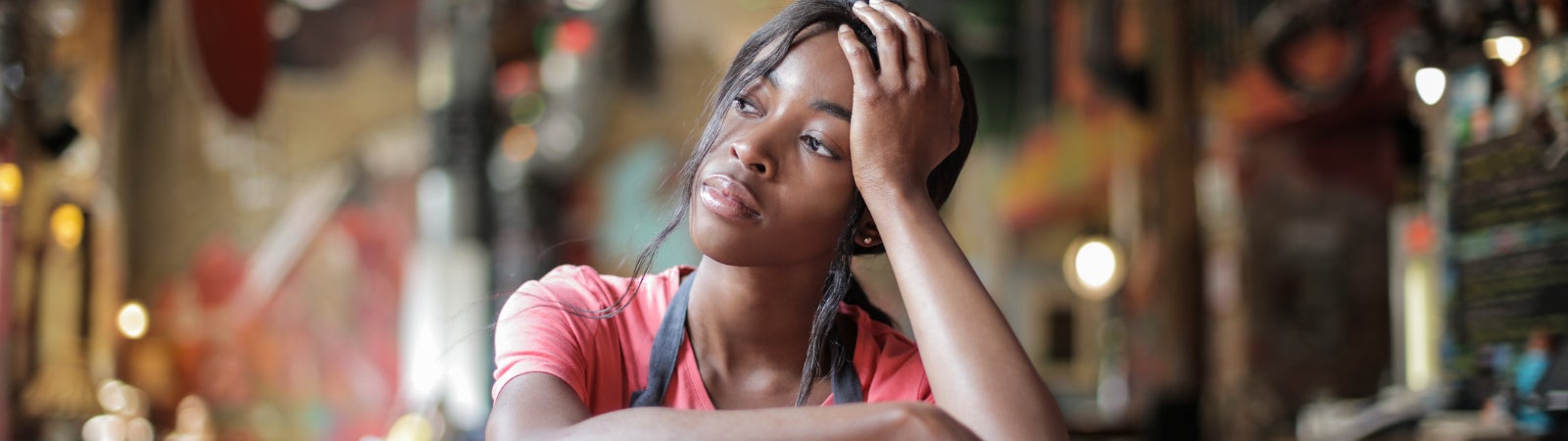 Restaurant worker sits in an empty restaurant, looking sad.
