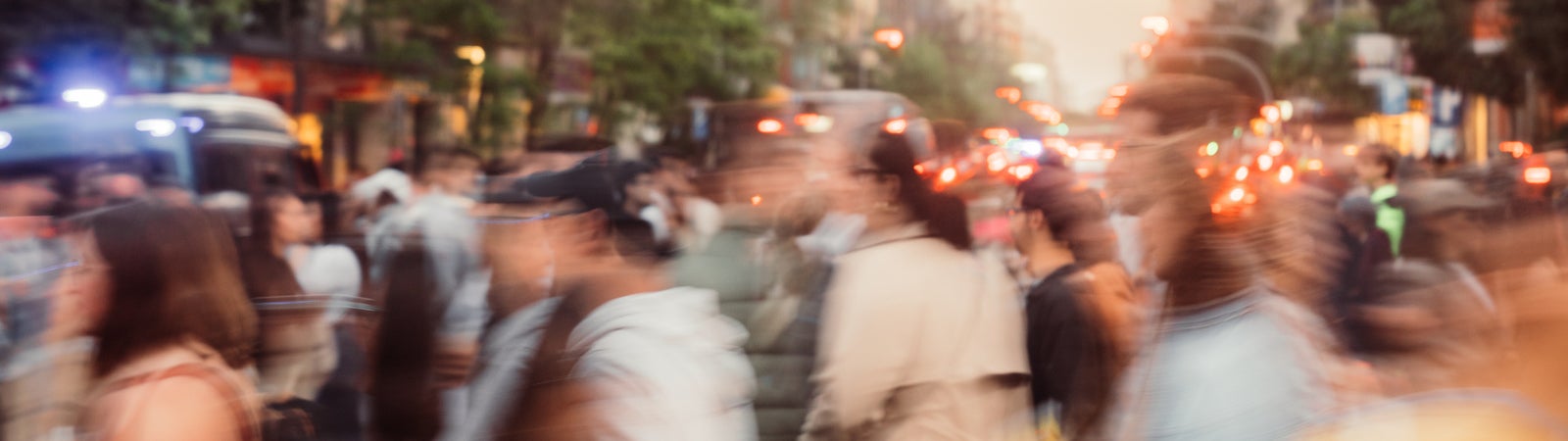 A photograph of a blurred crowd of people and cars on a busy city sidewalk.