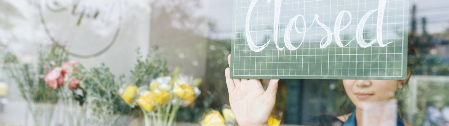 A woman puts a 'closed' sign on the door of her business.