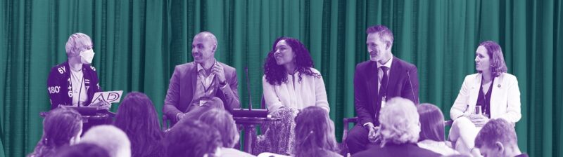 Colorized photo of a panel on stage in front of a crowd. The panel includes B Cavello, Zach Whitman, Victoria Houed, Travis Hoppe, and Katerina Antypas